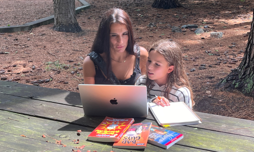 Mom and daughter sitting at a wooden table at the park with study materials