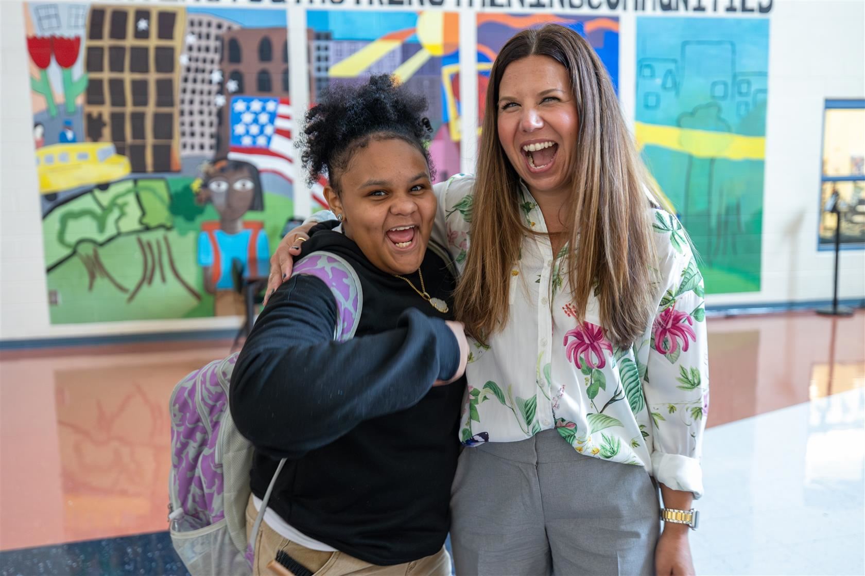 MLK Principal Jessica Savage smiles big with a student in front of a colorful mural