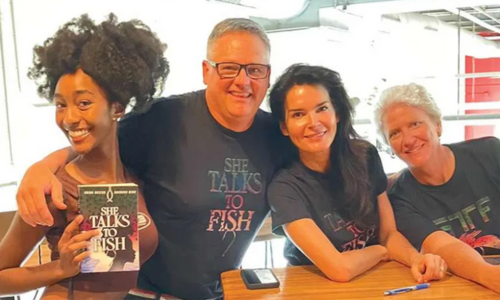 Book author Brian Hester stands at a table with three other people, smiling and posing with a book.